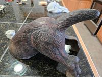 Side view showing the form and texture of the rear half of the dog sculpture with raised tail and visible metal wear.