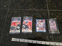 Four vintage hockey cards displayed on black tile floor with measuring tape below for scale. Two cards are sealed featuring Wayne Gretzky, one card of Kevin Lowe (New York Rangers), and one card of Mario Lemieux (Pittsburgh Penguins).