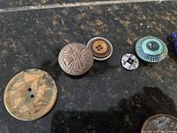 Close-up of six assorted buttons showing variety in material and design, including carved floral, wooden, and textured buttons