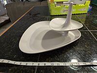 White two-tier triangular shaped serving tray with central post, shown with measuring tape for scale indicating around 13 inches width.