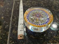 Side angle showing thickness of clear glass and colorful millefiori pattern inside, ruler included for scale.