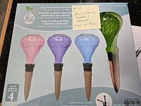 Box of four self watering plant globes in pink, purple, blue, and green with coral colored tapered tips shown in original packaging. Label shows English and French text.