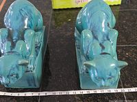 Front view of both cat sculptures on hearth with tape measure showing base length of approx 7 inches