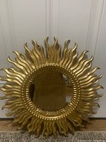Front view of the circular mirror with gold starburst frame showing flame-shaped protruding rays and beaded border around mirror.