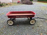 Photo of Henry Express red wagon side view on gravel showing the wagon body, wheels, and handle.