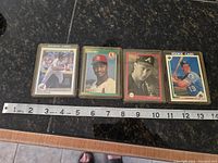 Four vintage baseball sports cards laid flat with measuring tape showing approximately 3x4 inches size each.