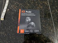 Front of the IQ Podz packaging showing product name, true wireless headphones, image of earbuds, Bluetooth logo, and 'No Wires, Just Fit' tagline.