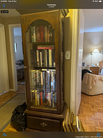 Full view of the tall wooden bookcase with glass front door and drawer at bottom. Filled with books.