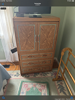 Wooden dresser with wood veneer patterned doors and drawers, metal handles, standing on wooden floor near a curtain.