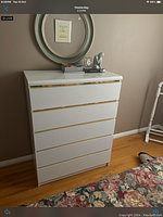 Photo of off white dresser against a taupe wall with 5 drawers and gold trim on edges, decorative items on top including books and a sculpture.