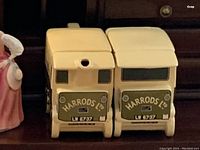 Front view of two cream-colored ceramic van-shaped items with Harrods Ltd. branding and license plate LV 6737, showing front grills and windows.