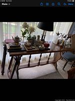 Photo of a large wooden hall table with spindle leg supports, located in front of a window. The table surface holds various decorative items which are not included in the sale.