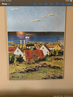 Framed painting or print of a coastal village with houses and ocean in background