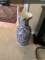 Decorative ceramic urn with blue background and white-green floral pattern, standing upright on carpet.