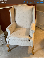 Front view of an off white wing tip chair with fabric upholstery and wooden cabriole legs.