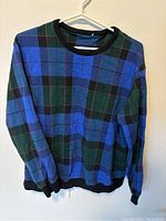Front view of a women's sweater in large size with a blue, green, and black plaid pattern and black ribbed cuffs and hem.