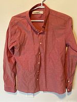 Salmon-colored long sleeved button-up shirt hanging on white hanger, front view
