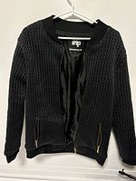 Front view of black textured bomber jacket hanging on white hanger