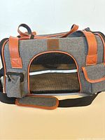 Front view of grey fabric cat carrier bag with orange-brown trim, mesh window, and pockets