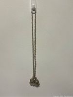 Full view of the two silver tone curtain tiebacks hanging against white wall, showing length and shape.