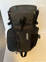 Full front view of the black Thule camera bag showing external pockets, straps, and 'Thule' logo.