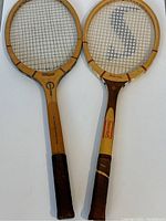 Two vintage wooden tennis rackets side by side, showing full frame and grip with worn leather handles.