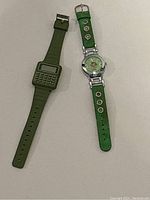 Both watches laid flat on a white surface showing the green calculator watch and the green strap monkey watch side by side.