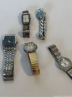Photo showing all five watches together, laid out on white surface, various styles and sizes evident.