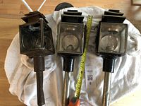 Photo of two antique carriage lights with cylindrical mounting stems and rectangular vented tops, placed on a white towel. One light shows wear and rust; the other is in better condition.