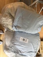 Photo shows two light blue fitted sheets, one mattress cover in plastic bag, and a king size lightweight bedspread on floor.