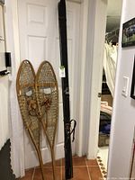 Pair of traditional wooden snowshoes and a black vintage ski leaning against a door.