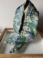 Ascot scarf displayed hanging showing paisley pattern and two-sided design with predominately green and blue colors.
