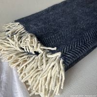 Close view of folded blanket showing navy and white herringbone weave and natural colored fringe
