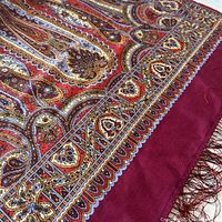 Close-up of scarf's intricate paisley pattern with cherry red, rust, creamy yellow, and blue colors showing detailed border and fringes.