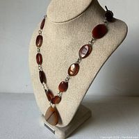 Full view of carnelian almond shaped bead necklace with teardrop pendant displayed on a stand.