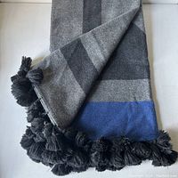 Folded grey and blue cashmere and wool throw showing tassels on one end and part of the color band.