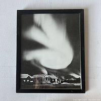 Front view of framed black and white Northern Ontario photograph showing houses, smoke, and sky with aurora effect.