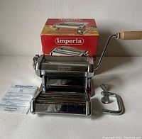 Front view of Imperia pasta maker with wooden handle, cutter attachment, clamp and instruction manual on display.