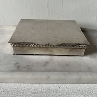 Closed silver plated box showing front and side with decorative edge trim and slightly tarnished silver finish.