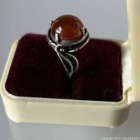 Front angled view of amber cabochon ring in cream and burgundy velvet case.