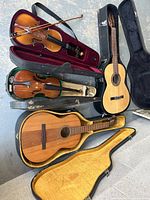 Top-down view showing two violins in open cases with bows and two acoustic guitars in open hard cases on floor.