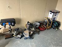 Bench drill press, three miter saws, gas compressor, hose reel, and crate with cords arranged against wall