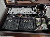 Pioneer DJ setup with two CDJ-700 units, DJ mixer, cables, headphones, and CDs on a desk surface.