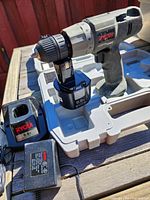 Ryobi cordless drill with black 3.6V battery attached shown in molded case insert along with 9.6V Ryobi charger and power adapter.