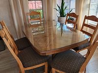 Photo showing the rectangular solid wood dining table with a glass top and six matching wooden chairs with patterned upholstered seats.