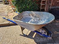 Side view of a Cobalt wheelbarrow showing metal tray with surface rust and blue frame with handles and pneumatic tire.