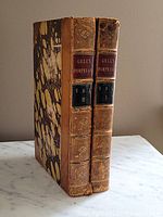 Two antique leather bound books standing upright with spines readable. Titles show Gell's Pompeiana Vol I and Vol II with marbled hard covers and leather spines.