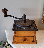 Full front view of antique wooden coffee grinder showing the crank handle, wooden base, and front drawer.