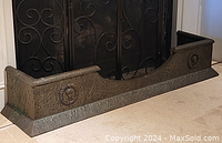 Full front view of the antique metal fireplace fender showing its length and placement against a fireplace.