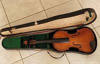 Violin and case fully opened showing violin placed inside the case with unstrung strings and brown leather strap